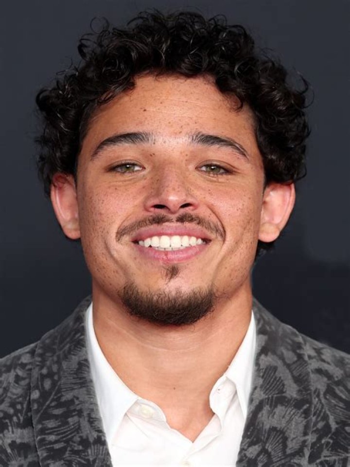 Anthony Ramos smiling in a white t-shirt and white jacket.